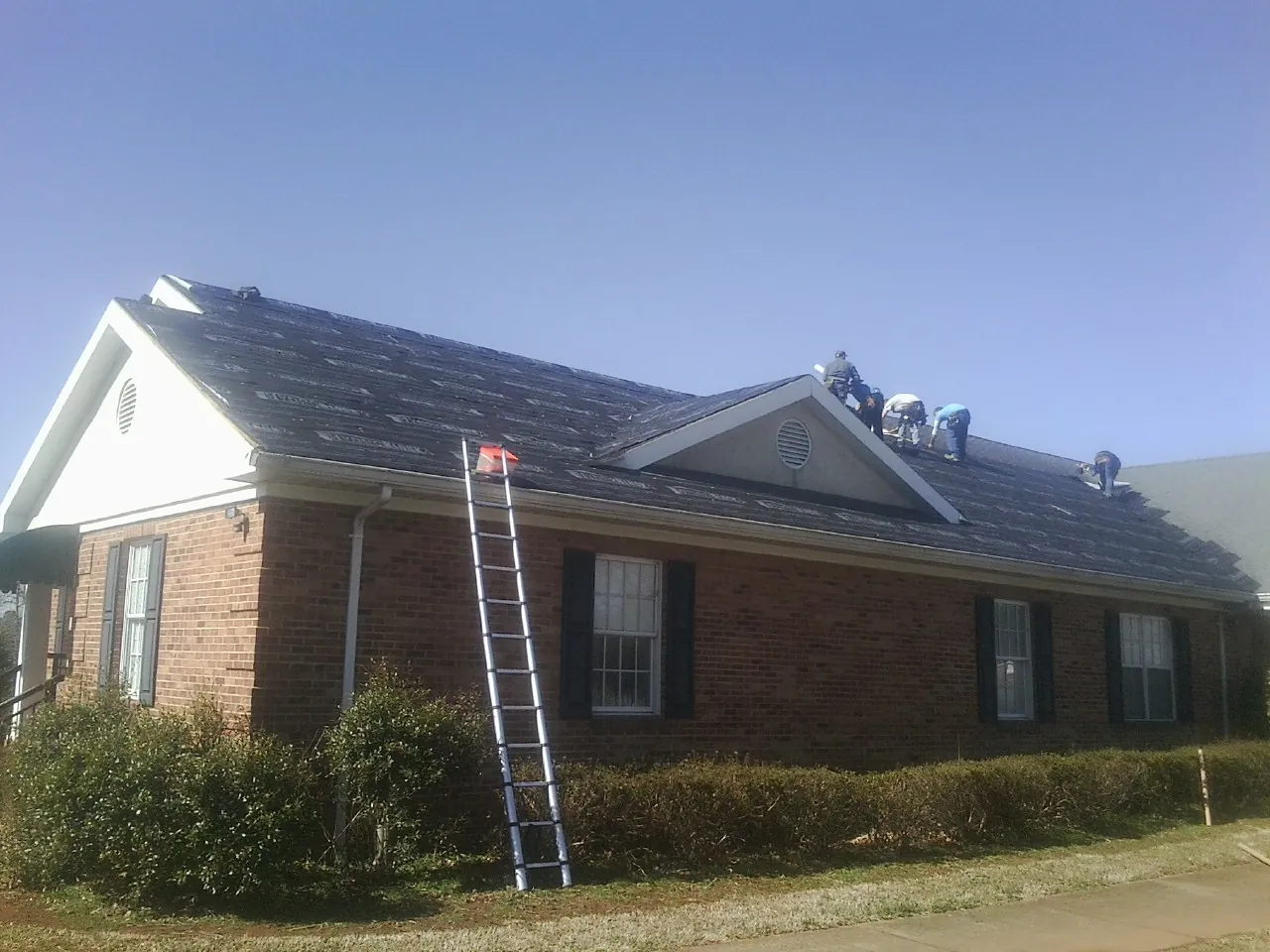 Crew tearing shingles off a brick ranch roof with a ladder set — Metal Roof Repair work by our crew in Ruckersville