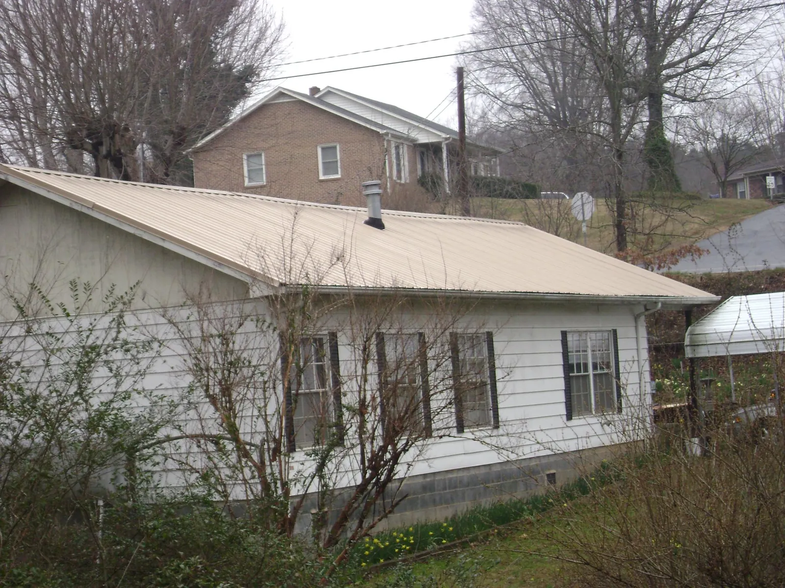 Tan metal roof on a white sided house set into a hillside — Commercial Roofing by Roofing Brothers in Ruckersville